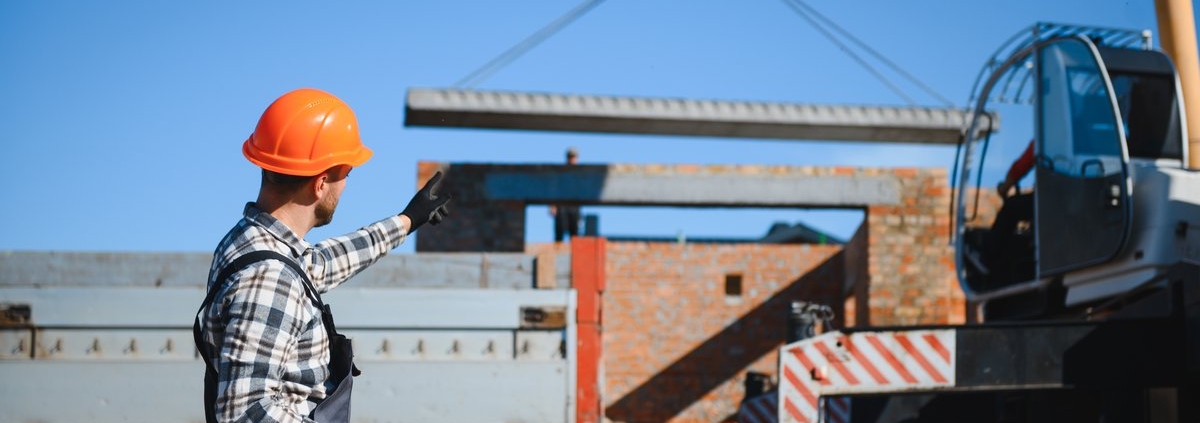 Camion-grue avec bras déployé et chauffeur-opérateur levant une charge lourde sur un chantier